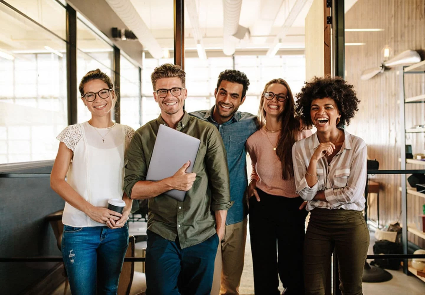 Eine Gruppe von vier fröhlichen Mitarbeitern steht zusammen in einem Büro