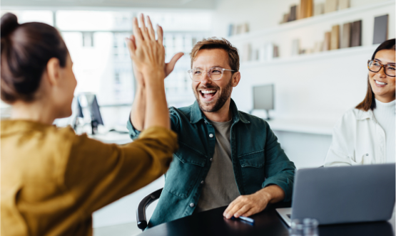 Fröhliche Mitarbeiter feiern ihre Leistung mit einem High-Five in einer modernen Büroumgebung