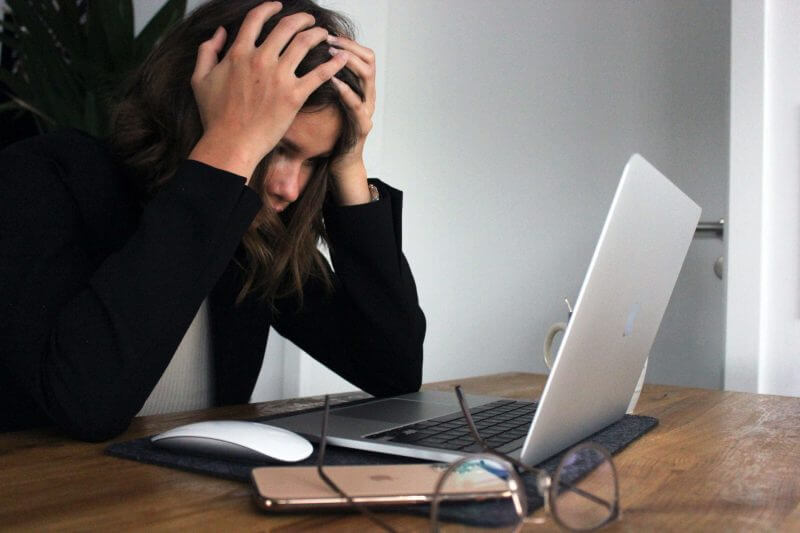 Eine Frau sitzts verzweifelt und mit den Händen am Kopf vor ihrem Laptop