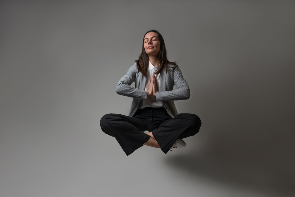 Eine Junge Frau in einem formellen Anzug sitzt im Schneidersitz und levitiert in einer Meditationshaltung